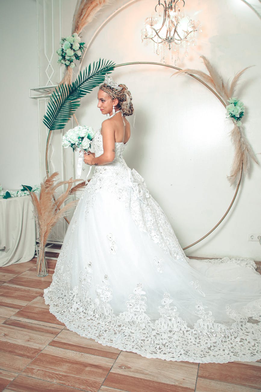 A stunning bride in a lace wedding dress with a tiara poses indoors with a bouquet, creating a fairytale wedding look.