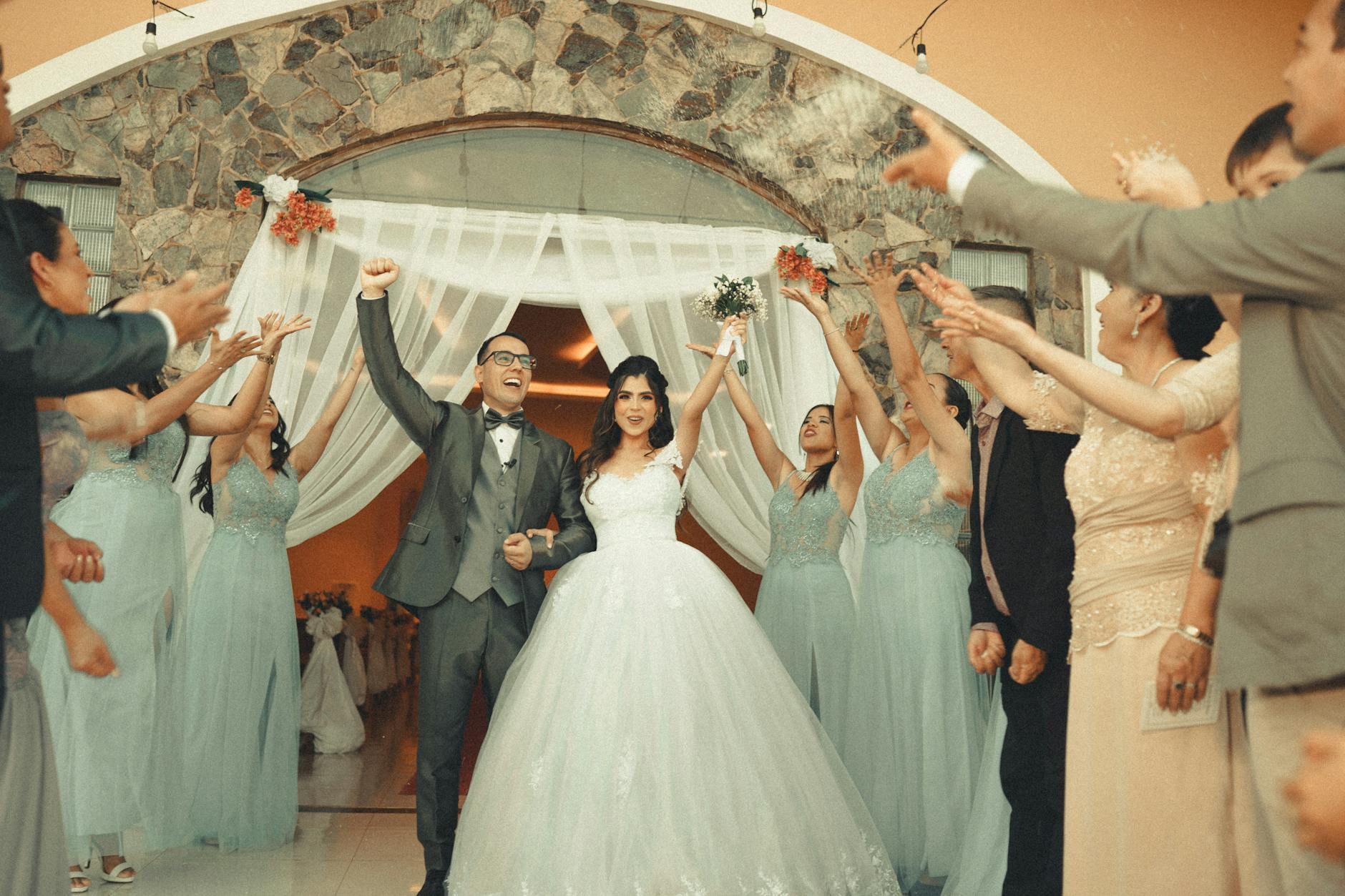 Cheerful newlyweds celebrating their wedding with guests applauding in stylish attire.