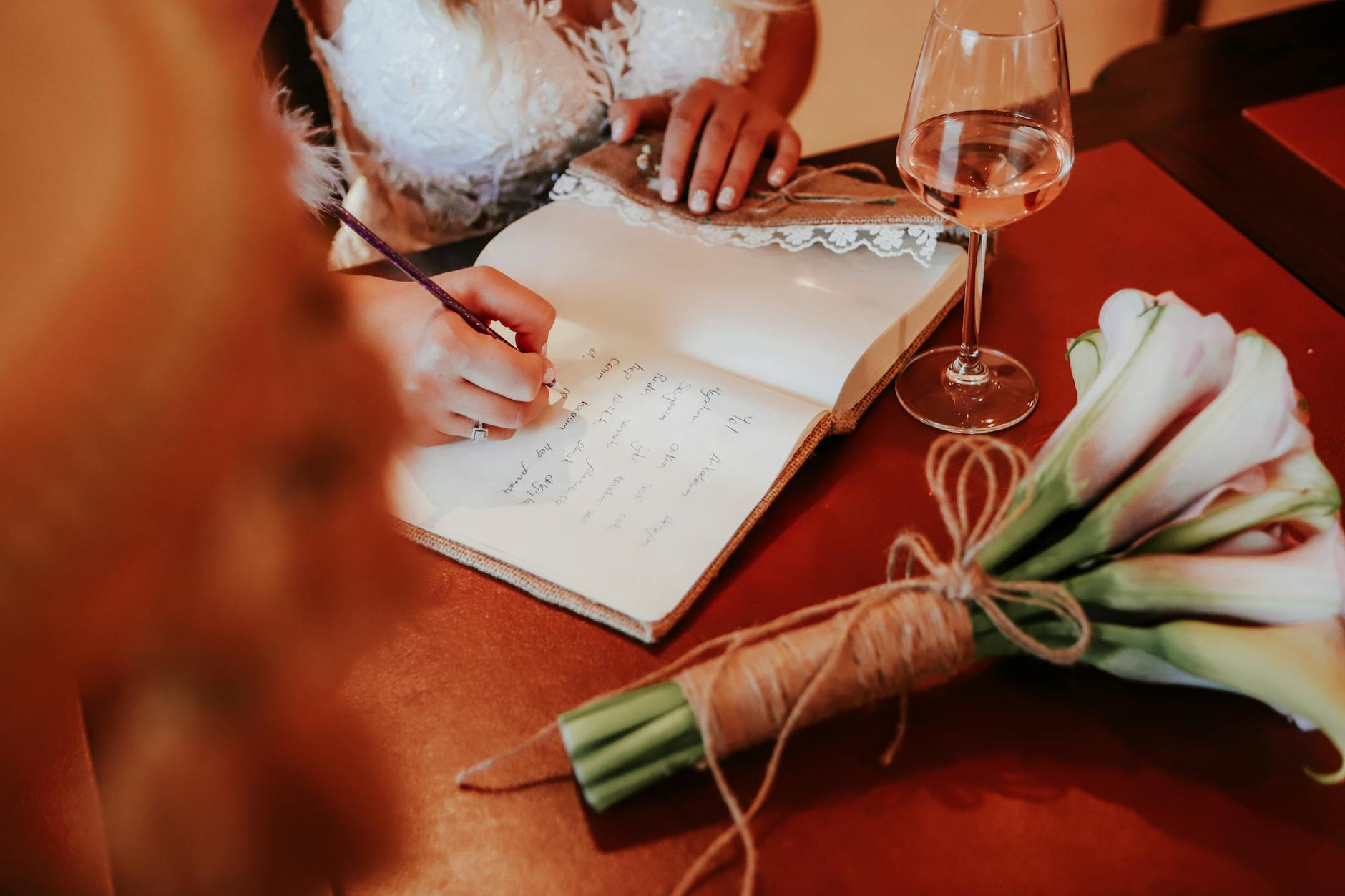 Bride writes in a journal with a bouquet and wine glass, capturing a serene wedding moment.