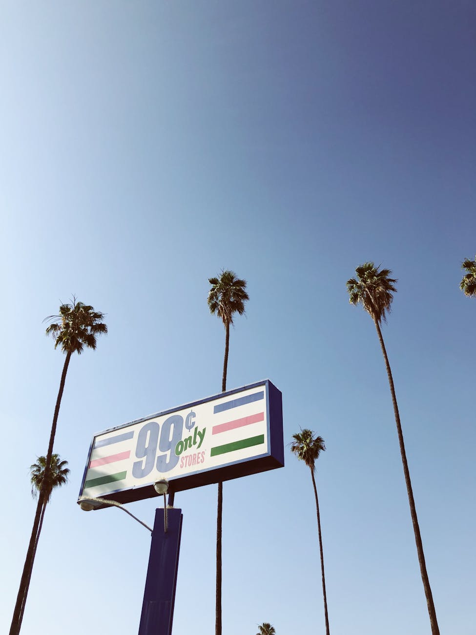 99 Cents Only Store sign under a clear blue sky with tall palm trees.