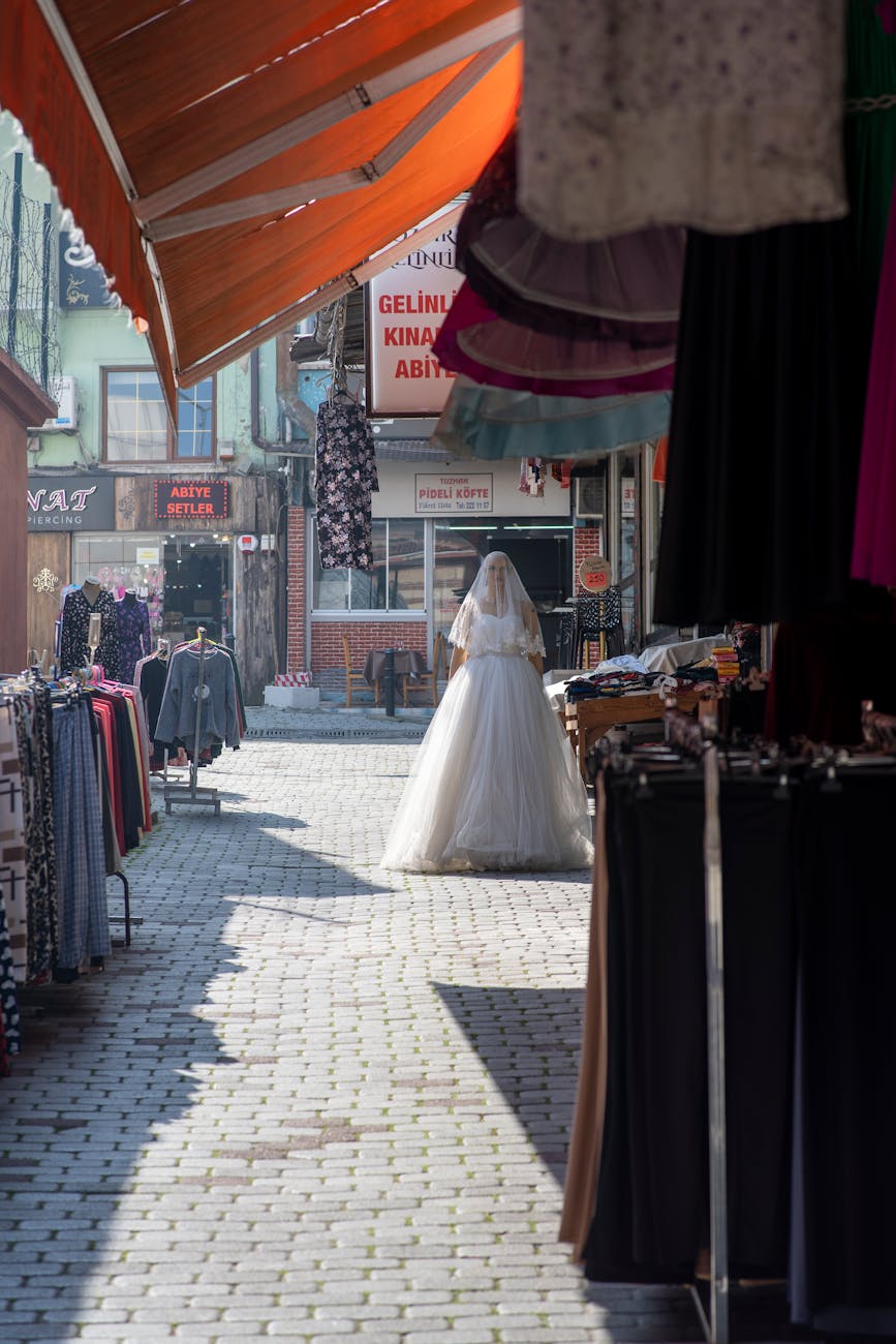 A bride walks through a quaint bazaar in Bursa, Türkiye, surrounded by vibrant market stalls.
