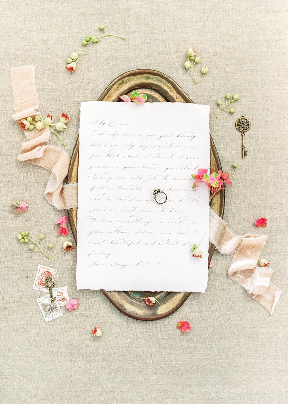 Romantic flat lay featuring a handwritten letter with flowers, ribbon, and an antique key on a brass tray.